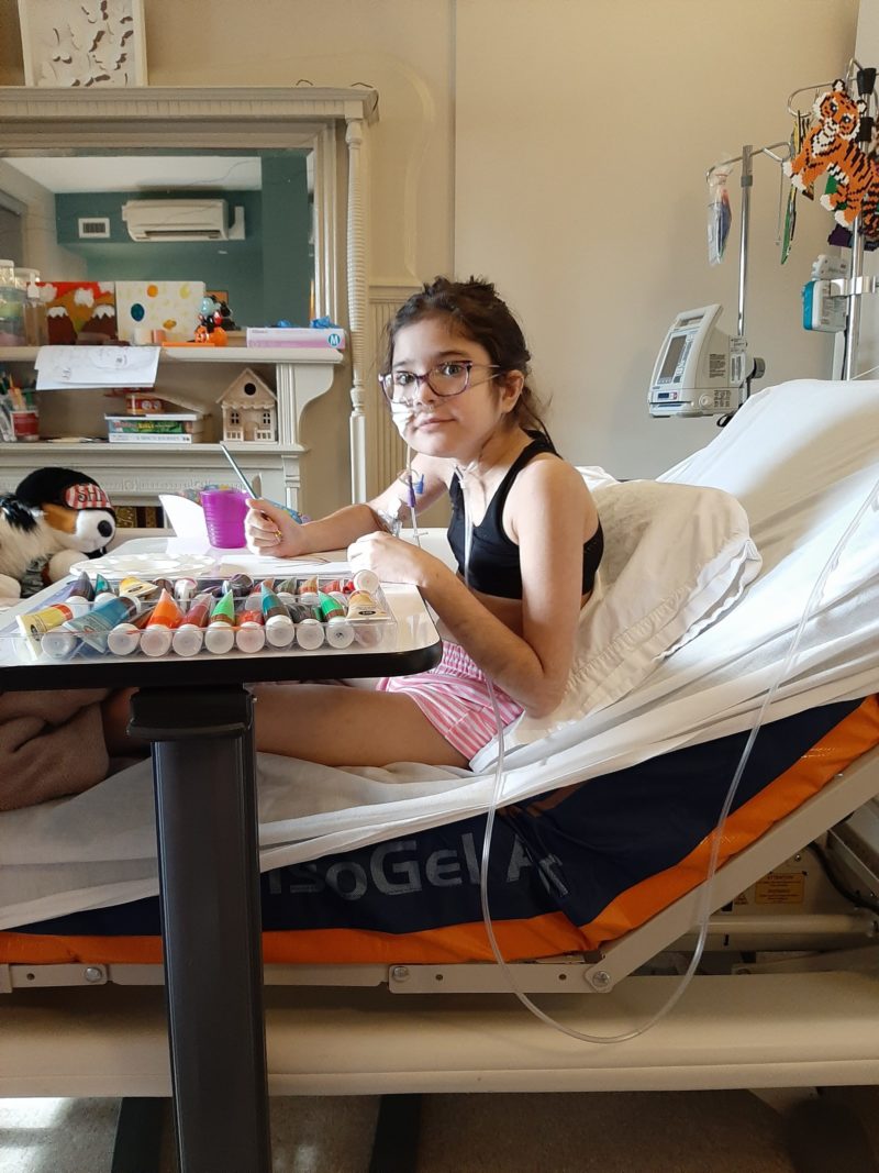 Tanika, an Emily’s House child in her hospital bed, deeply engaged in a Recreation Program craft activity