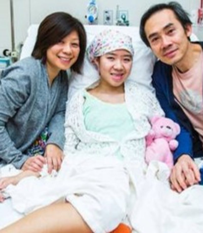 A photo of Cassidy in a hospital bed, where she is accompanied by her mom and dad. All three are smiling