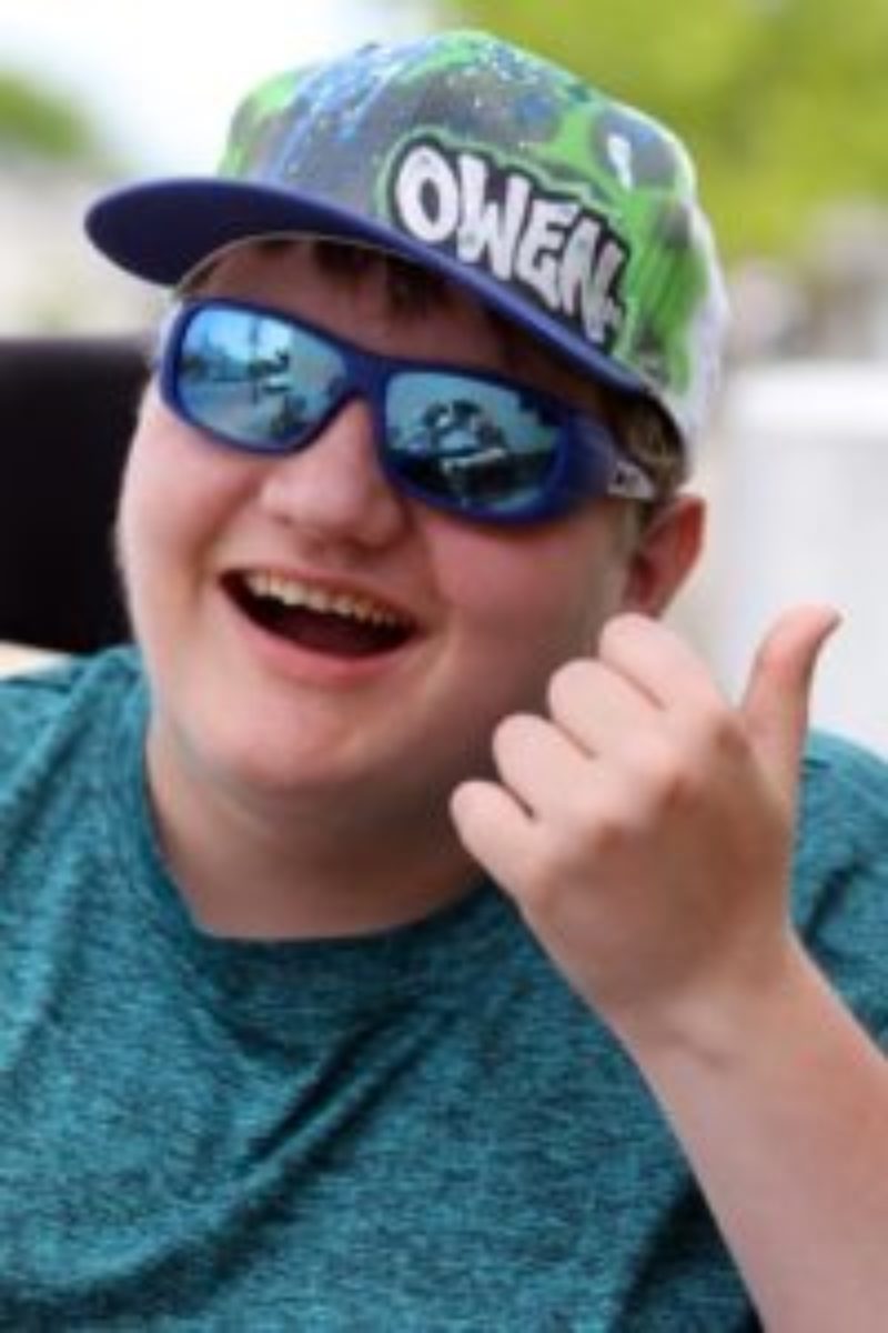 Photo of Owen smiling as he gives a thumbs up from his wheelchair