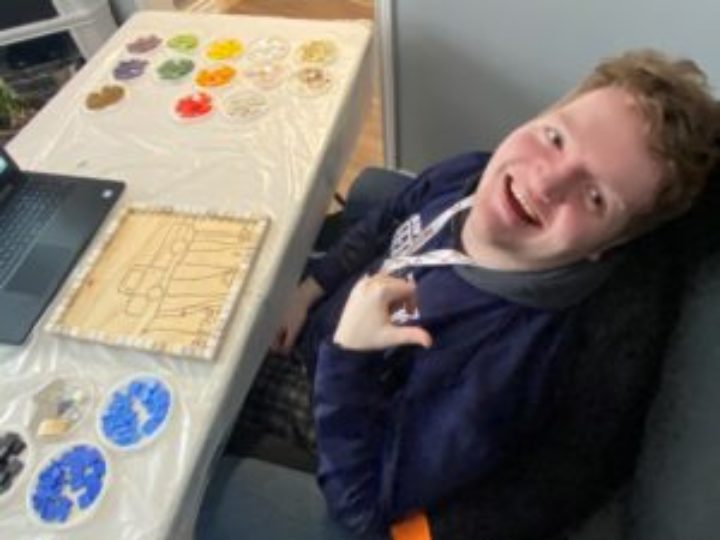 Photo of Owen creating his contribution to the Emily’s House tile mosaic, as he sits at a desk participating in the zoom recreation session