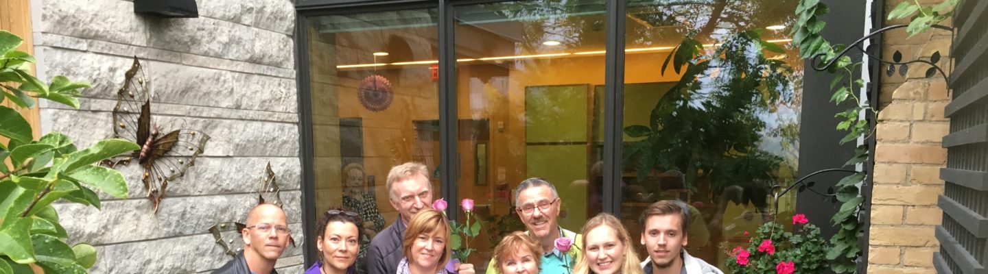 An Emily’s House family gathers in Ava‘s Garden on the west side of the Emily’s House building, with purple roses in memory of a child